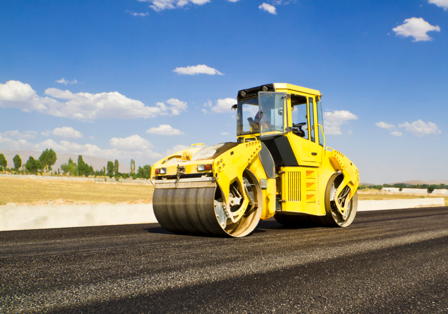 Yellow roller flattening fresh tarmac on a road, blue sky behind